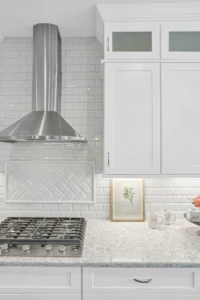 Bright modern white kitchen with quartz countertops, stainless steel appliances, and herringbone tile backsplash.