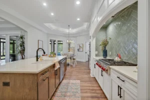 Bright modern kitchen with white cabinets, wood floors, quartz island, and open dining area.