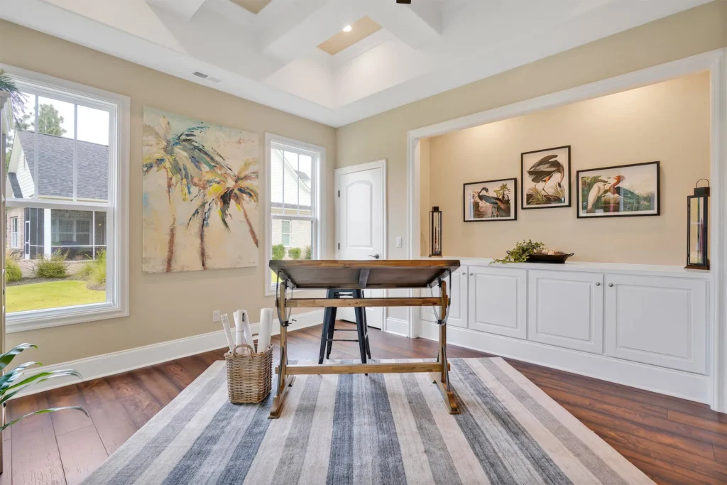 Bright coastal home office with wooden desk, natural light, and tropical wall art.