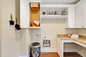 Modern beige laundry room with white cabinets, dark flooring, and organized cleaning essentials.