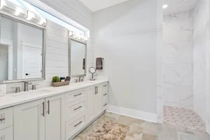 Bright modern bathroom with dual vanity, marble walk-in shower, and elegant cream cabinetry.