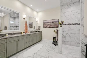 Modern marble bathroom with sage green vanity, glass shower, and elegant lighting.