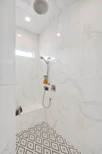 Luxurious marble walk-in shower with rainfall and handheld fixtures, bench, and geometric tile floor.