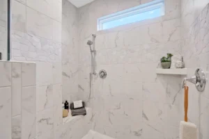 Modern marble walk-in shower with chrome fixtures, built-in bench, and bright spa-like lighting.