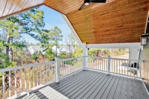 Modern covered deck with vaulted wood ceiling, ceiling fan, and scenic suburban tree-lined view.