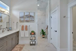 Modern bathroom with double vanity, marble walk-in shower, and coral accents in neutral tones.