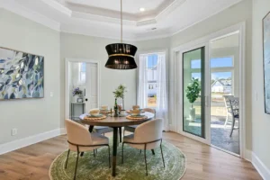 Elegant modern dining room with round table, beige chairs, green rug, and black pendant light.