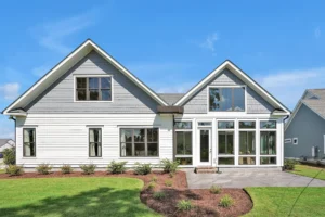 Modern gray farmhouse with gabled roofs, white trim, and large windows under a bright blue sky.