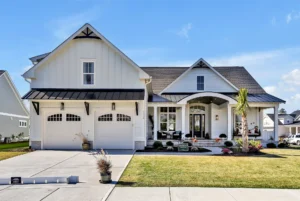 Modern white farmhouse with black accents, front porch, two-car garage, and bright suburban landscaping.