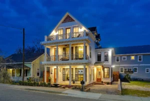 Elegant three-story modern home illuminated at twilight with balconies, warm lighting, and gable roof.