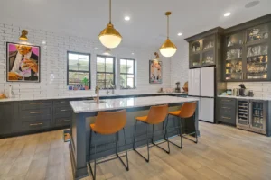Modern gray kitchen with white quartz island, gold lighting, and caramel leather bar stools.
