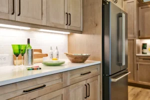 Modern light wood kitchen with white countertops, black handles, and warm ambient lighting.