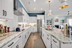 Modern white kitchen with marble island, gold pendant lights, and warm wood flooring.
