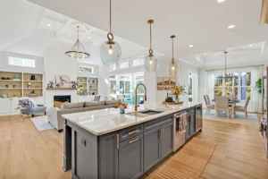 Modern open-concept kitchen with gray island, light oak floors, and bright living-dining area.
