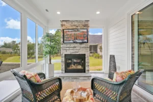 Bright sunroom with stone fireplace, wicker chairs, and natural light overlooking lush green views.