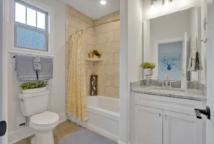 Bright modern bathroom with beige tones, yellow shower curtain, granite vanity, and natural light.