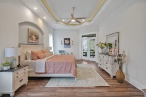 Elegant master bedroom with tray ceiling, warm lighting, peach bedding, and modern wooden accents.