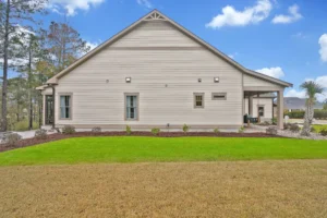 Modern single-story farmhouse with cream siding, gable roof, covered porch, and manicured lawn.
