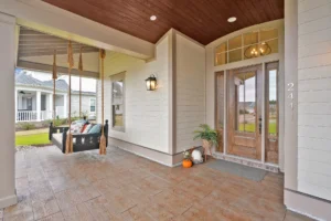 Welcoming front porch with wood ceiling, swing bench, and elegant glass-paneled door.