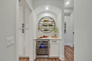 Modern hallway home bar with circular shelves, quartz countertop, wine cooler, and warm lighting.