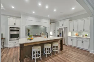 Modern white kitchen with large island, wood accents, and stainless steel appliances.