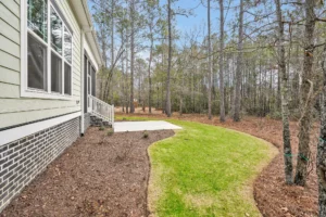 Modern Wilmington backyard with curved lawn, fresh mulch, patio, and wooded privacy backdrop.