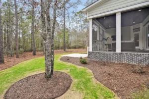 Screened porch with landscaped backyard, green lawn, mulch beds, and wooded view in Wilmington.