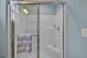 Modern glass shower with silver frame and gray elephant towel in bright minimalist bathroom.