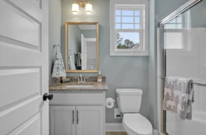 Bright coastal bathroom with white vanity, glass shower, gray-blue walls, and wood-look flooring.