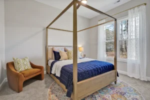Modern minimalist bedroom with wooden canopy bed, navy and cream decor, and natural sunlight.