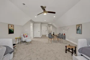 Spacious attic bonus room with gray walls, beige carpet, cozy seating, and a functional workspace.