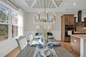 Elegant dining room with coffered ceiling, gold chandelier, and modern kitchen in warm neutral tones.