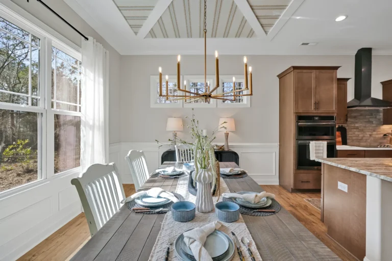 Elegant dining room with coffered ceiling, gold chandelier, and modern kitchen in warm neutral tones.