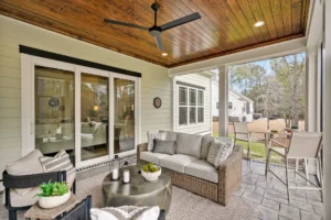 Modern enclosed patio with wood ceiling, wicker seating, and bar overlooking a lush green yard.