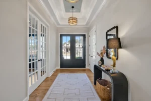 Modern entryway with black double doors, wood flooring, tray ceiling, and gold pendant lighting.
