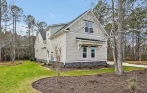 Modern two-story farmhouse with light siding, stone accents, and pine trees in a serene setting.