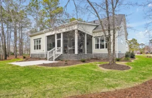 Single-story home with screened porch, light siding, and landscaped yard surrounded by mature trees.
