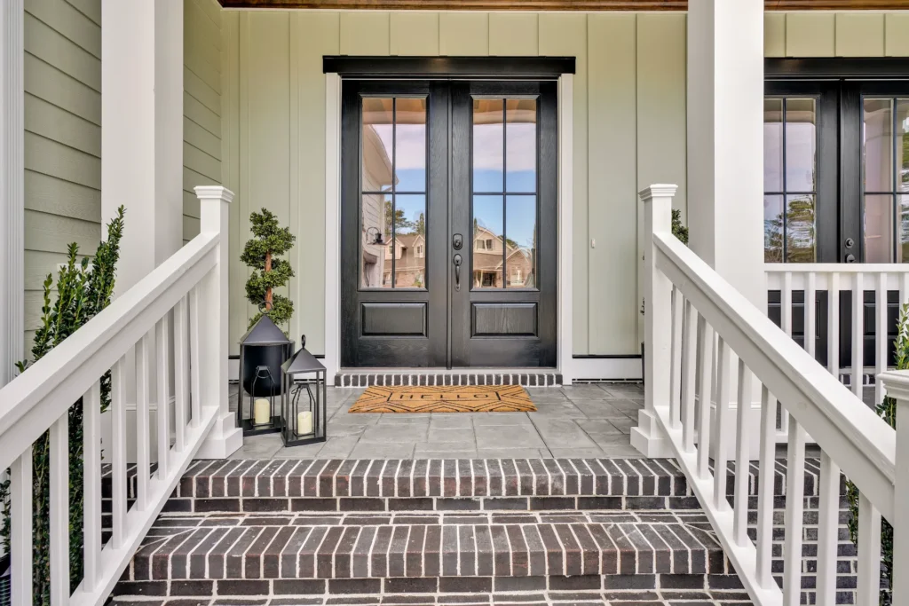 Modern front porch with black double doors, white trim, brick steps, and potted plants.