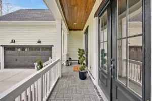 Modern front porch with black double doors, wood ceiling, and spiral plant by welcoming entryway.