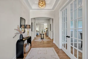 Modern hallway with light wood floors, gold chandelier, black console table, and natural light.
