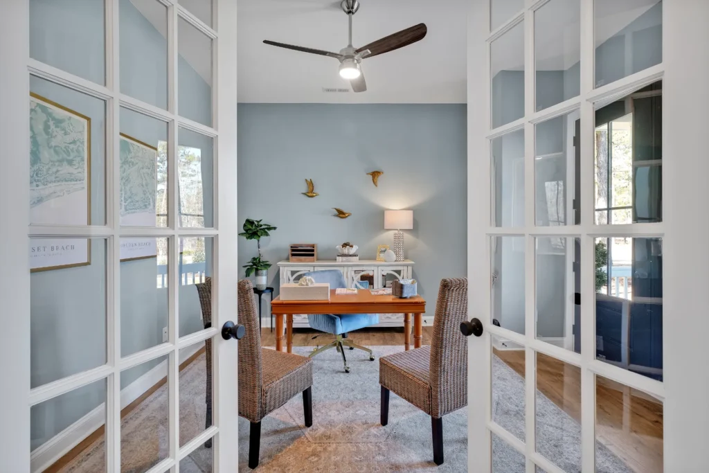 Bright light blue home office with golden bird accents, wooden desk, and woven chairs.