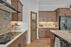 Modern kitchen with warm wood cabinets, stone backsplash, light countertops, and central island.