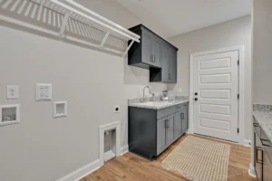 Modern laundry room with gray cabinets, wood floors, and light granite countertop.