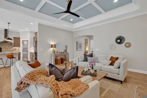 Modern open-concept living room with coffered ceiling, light sofas, and warm contemporary decor.