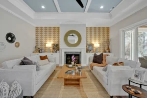 Modern living room with white fireplace, gold mirror, gray sofas, and warm natural lighting.