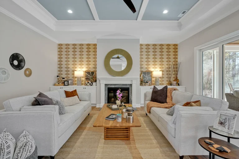 Modern living room with white fireplace, gold mirror, gray sofas, and warm natural lighting.