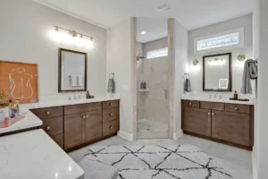 Modern master bathroom with double vanities, glass walk-in shower, dark wood cabinets, and elegant lighting.