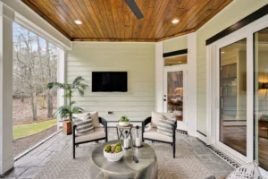 Modern outdoor patio with wood ceiling, cushioned seating, coffee table, and relaxing natural surroundings.