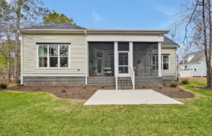 Rear view of modern single-story home with screened porch, concrete patio, and landscaped backyard.