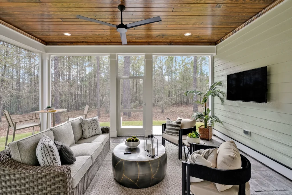 Modern screened porch with wood ceiling, glass walls, and cozy neutral seating overlooking nature.